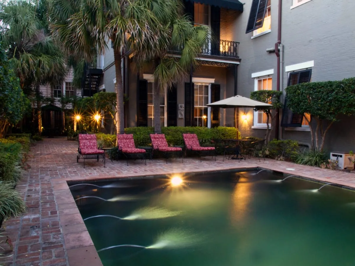 Brick courtyard pool at dusk with lounge chairs and an umbrella