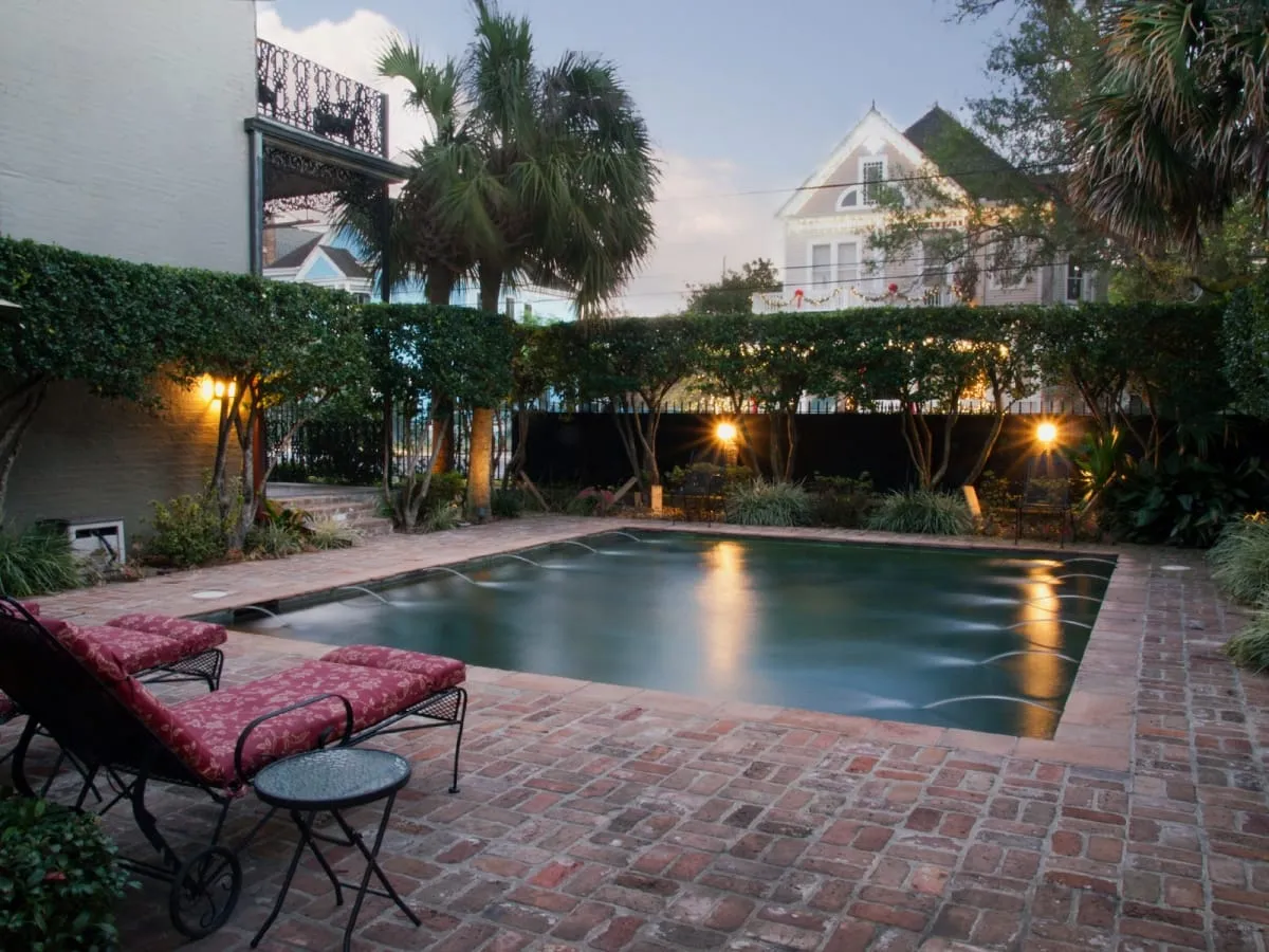 The pool and brick patio at dusk with red chaise lounges and a glass conservatory beyond