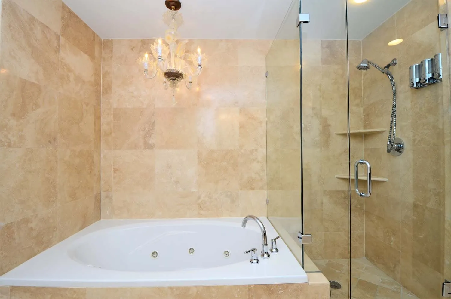 Jetted tub and glass shower under a chandelier